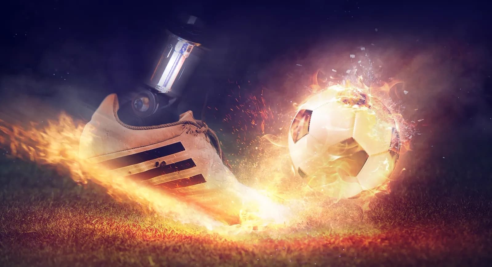 A digitally composited football boot striking a ball, both wreathed in flame, above floodlit grass at night.
