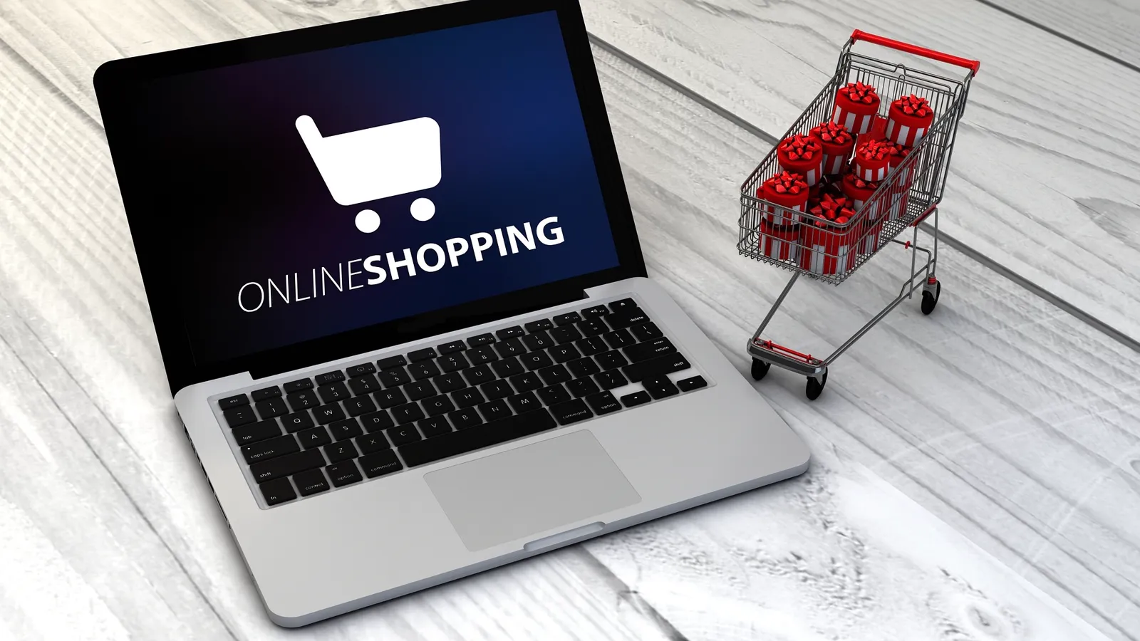 An open laptop showing an online shopping screen, beside a toy shopping trolley loaded with small wrapped gifts.